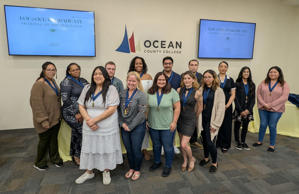 A group of students posing as a group in front of two TVs and the OCC logo