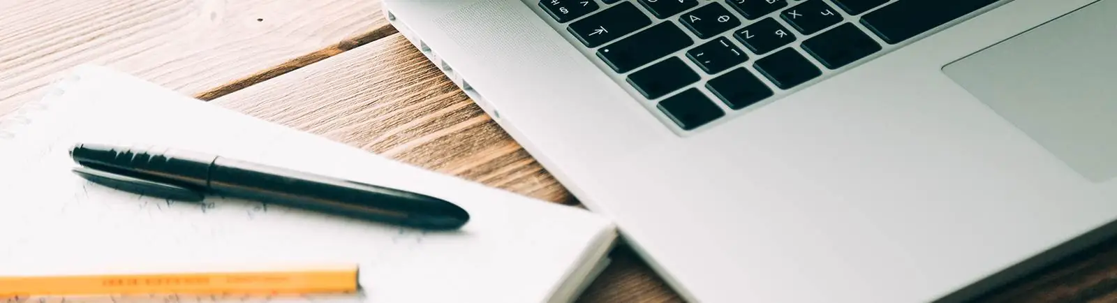 close up of a pad of paper, pens and laptop