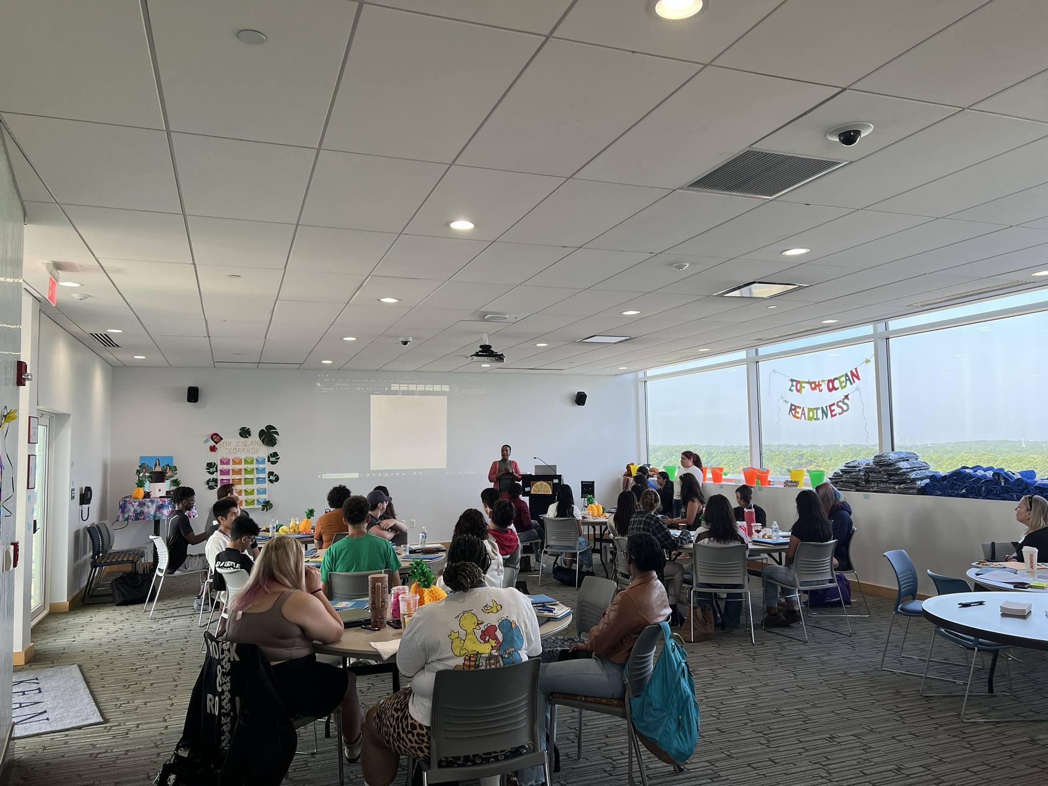 Photo of a classroom filled with students at tables watching a presentation. 